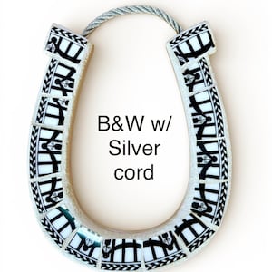 May include: A decorative horseshoe with a mosaic design in black and white, featuring a silver cord for hanging. The horseshoe has the text "B&W w/ Silver cord" on it.