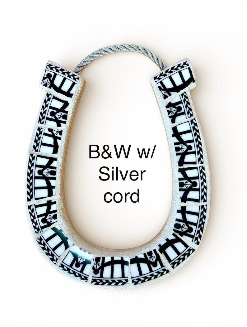 May include: A decorative horseshoe with a mosaic design in black and white, featuring a silver cord for hanging. The horseshoe has the text "B&W w/ Silver cord" on it.