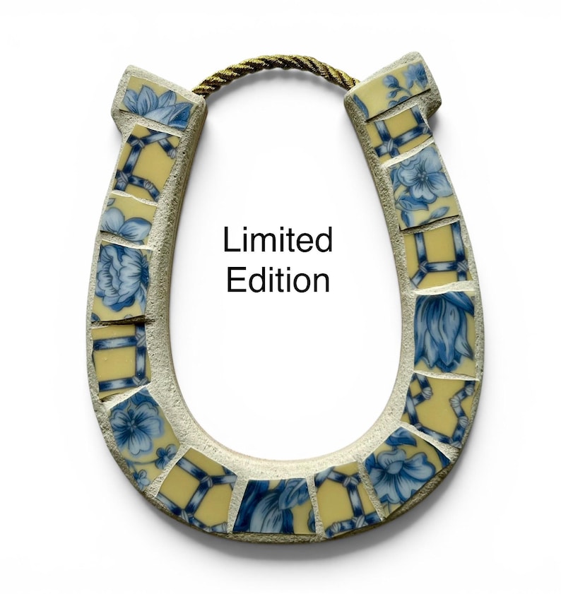 May include: A horseshoe-shaped wall hanging with a mosaic design. The mosaic features blue floral patterns on yellow tiles, set within a light-colored frame. The text "Limited Edition" is displayed on the front. A gold rope is attached at the top.