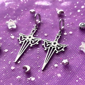 Peut inclure: Une paire de boucles d'oreilles en argent en forme de poignard avec des détails complexes. Les poignards ont un motif d'étoile et de croissant de lune.