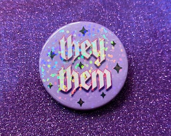 Peut inclure: Bouton violet avec des paillettes et des étoiles noires. Le bouton dit "they them" en lettres blanches avec un contour rose.