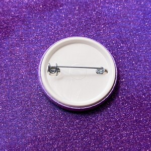 May include: The back of a purple button with a metal pin and clasp.