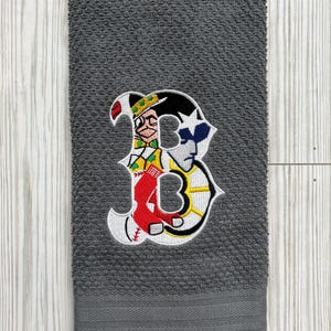Puede incluir: Toalla de cocina gris con un logotipo de béisbol bordado que presenta una "B" roja, blanca, azul y amarilla con un personaje de dibujos animados en su interior.