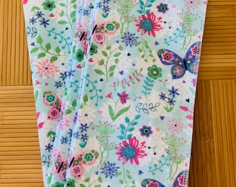 May include: A stack of four blue and white fabric napkins with a floral and butterfly pattern. The napkins are folded in half and have a white background with pink, blue, and green flowers and butterflies.