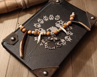 May include: A necklace featuring a central black wolf head pendant, flanked by two long brown antler-like pieces and white tusk-shaped beads. The strand consists of round wooden beads in tan and brown, with some beads displaying small black circular symbols.
