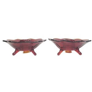 May include: A pair of red glass candle holders with three legs each. The holders have a scalloped edge and a gold rim.