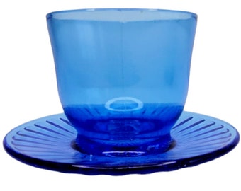 May include: A blue glass teacup and saucer set. The cup and saucer have a fluted design.