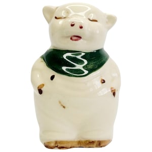 Puede incluir: Una alcancía de cerámica blanca con un pañuelo verde. La alcancía tiene detalles pintados en marrón y la boca cerrada.