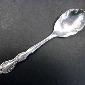 May include: A silver sugar spoon with a decorative handle and a scalloped edge.