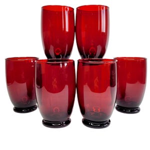 Peut inclure: Ensemble de six verres à boire rouge rubis. Chaque verre a un corps arrondi et une base sombre. Les verres sont disposés en deux rangées, avec trois verres dans chaque rangée. Les verres sont en matériau transparent.