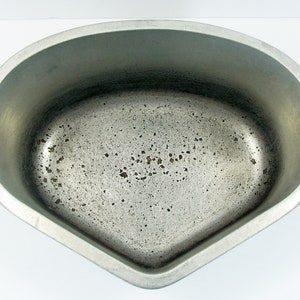 Puede incluir: Un molde para hornear ovalado de aluminio plateado con dos asas. El molde tiene una superficie texturizada y muestra signos de uso.