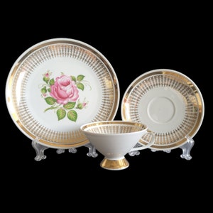 May include: A vintage tea set featuring a white teacup, saucer, and plate with gold trim and a pink rose design. The set includes a teacup, a saucer, and a plate, all with a gold filigree pattern.