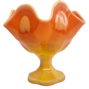 Op de afbeelding: Een vintage oranje en gele glazen kom met een gerimpelde rand. De kom heeft een voetstuk en een glanzende afwerking. De kleurovergang verloopt van een levendig oranje aan de bovenkant naar een zacht geel aan de basis.