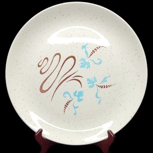 May include: A white ceramic dinner plate with a speckled glaze. The plate features a brown and blue floral design.