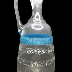 May include: A clear glass pitcher with a blue band and white floral design. The pitcher has a round body and a curved handle.