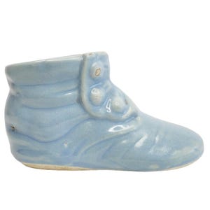 Könnte beinhalten: Ein hellblauer Keramik-Babyschuh-Pflanztopf. Der Schuh hat ein Knopfdetail und eine leicht spitze Spitze.