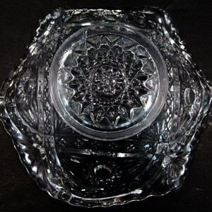 May include: A clear glass bowl with a cut glass design. The bowl has a scalloped edge and a starburst pattern in the center.