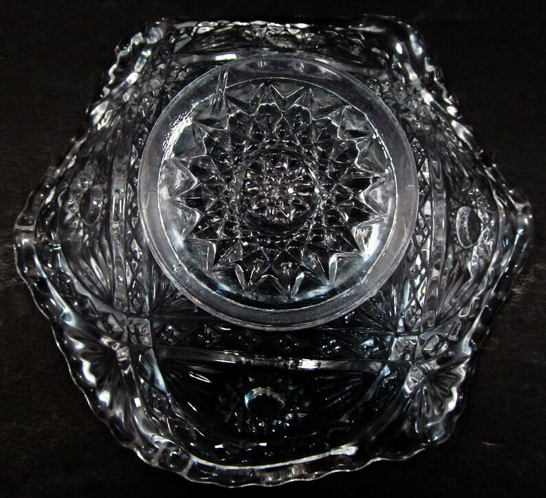 May include: A clear glass bowl with a cut glass design. The bowl has a scalloped edge and a starburst pattern in the center.