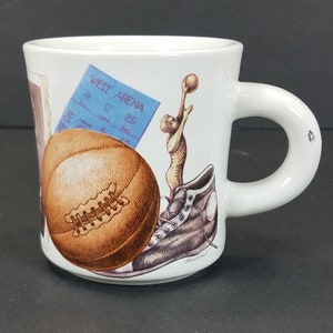 Op de afbeelding: Witte keramische mok met een basketbal, een basketbalschoen, een ticketstub met de tekst "West Arena" en een cartoonbasketbalspeler. De mok heeft een handvat.