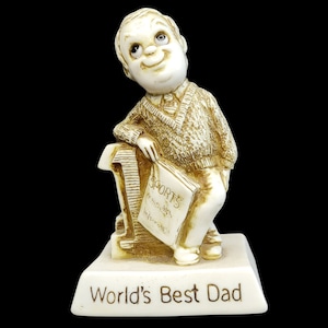 Può includere: Una statuetta in ceramica bianca di un uomo che tiene un libro che dice "Sports" e seduto su un piedistallo che dice "World's Best Dad".