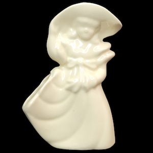 Könnte beinhalten: Weiße Keramikfigur einer Frau mit Hut und Kleid. Die Frau hält einen Blumenstrauß in der Hand. Die Figur ist als Pflanzgefäß gedacht.