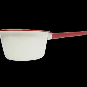 May include: A white enamel saucepan with a red rim and handle. The saucepan has a long, straight handle and a rounded body. The red handle and rim provide a striking contrast to the white enamel.