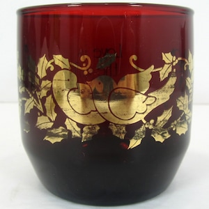 May include: A red glass tumbler with a gold design of two birds and holly leaves. The birds are facing each other and are surrounded by holly leaves and berries.
