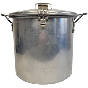 Puede incluir: Un recipiente cilíndrico de metal plateado con tapa y cierre de bisagra. El recipiente tiene dos asas y probablemente se utiliza para almacenamiento. La tapa se asegura con un cierre metálico. El recipiente es de metal cepillado.