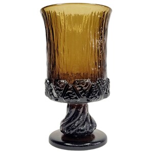 May include: A brown glass goblet with a textured tree bark design. The goblet has a black base with a twisted tree trunk design.