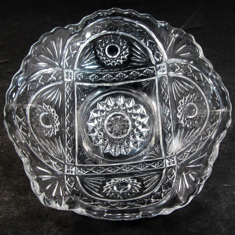 May include: A clear glass bowl with a scalloped edge and intricate cut-glass design. The bowl features a central circular pattern surrounded by four smaller circular patterns.