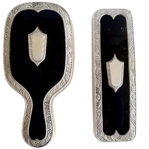 May include: A vintage silver-plated hand mirror and hairbrush set with black enamel and a silver shield design.