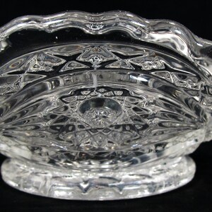 May include: A clear glass bowl with a scalloped edge and a decorative pattern. The bowl has a footed base.