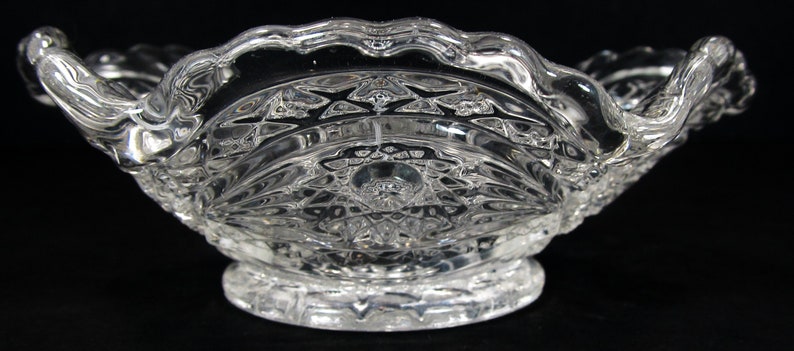 May include: A clear glass bowl with a scalloped edge and a decorative pattern. The bowl has a footed base.
