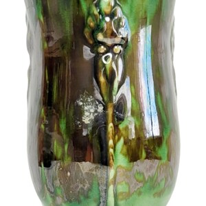 May include: A green and brown ceramic vase with a raised floral design. The vase has a wide base and a narrow neck.