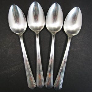 Peut inclure: Quatre cuillères en argent disposées sur un fond sombre. Les cuillères ont un bol ovale et un long manche avec un motif décoratif. Elles reflètent la lumière, créant un aspect brillant. Un ensemble classique pour la table.