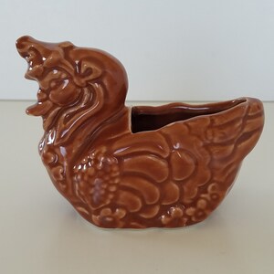 Op de afbeelding: Een bruine keramische plantenpot in de vorm van een eend met gedetailleerde veren en een textuur.
