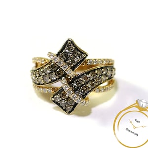 Puede incluir: Un anillo de oro con una piedra central de diamante marrón y diamantes marrones más pequeños que la rodean. El anillo está engastado en un diseño de banda retorcida.