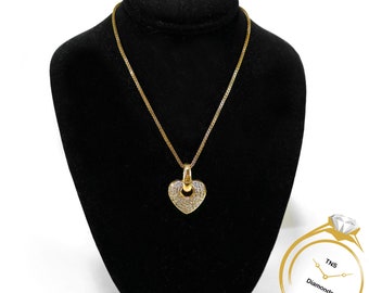 Puede incluir: Un collar de oro con un colgante en forma de corazón adornado con pequeñas piedras transparentes. El collar está sobre un expositor de terciopelo negro.