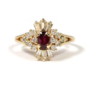 Puede incluir: Un anillo de oro con una piedra preciosa de rubí rojo rodeada de un grupo de diamantes más pequeños.