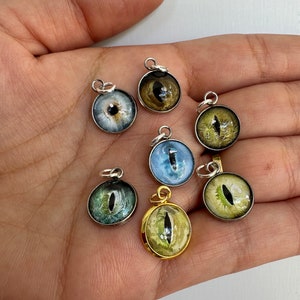 May include: Seven different eye charms, each with a unique color and design. The charms are round and have a silver or gold setting. The eyes are all different colors, including blue, green, and brown.