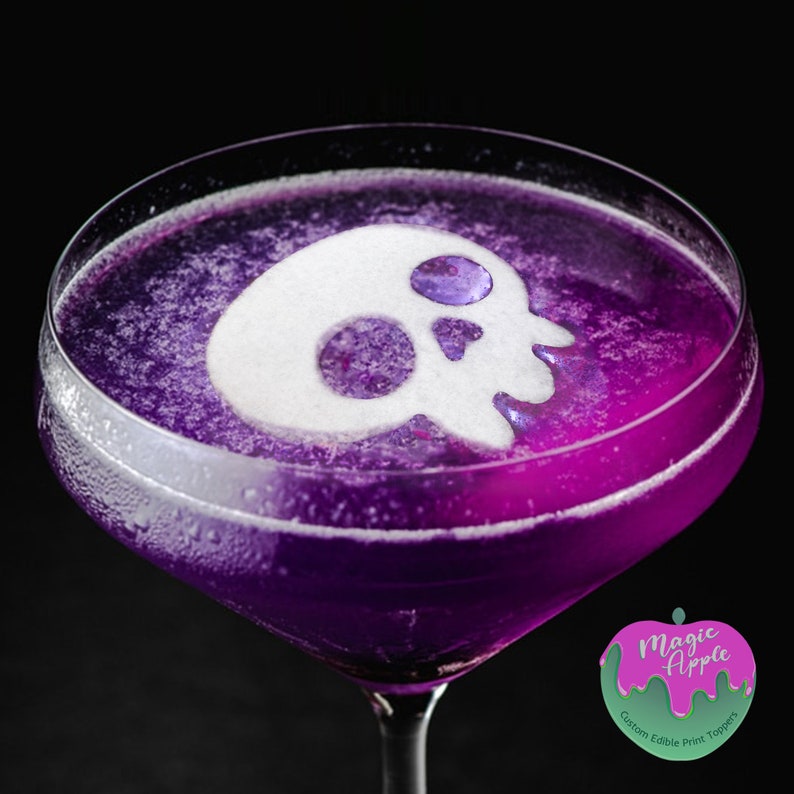 May include: A purple cocktail with a white sugar skull on top. The cocktail is in a martini glass. The image has a logo for "Magic Apple Custom Edible Print Toppers" in the bottom right corner.