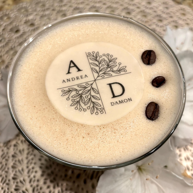 May include: A white round cake topper with black lettering and a floral design. The topper says "A Andrea" and "D Damon".