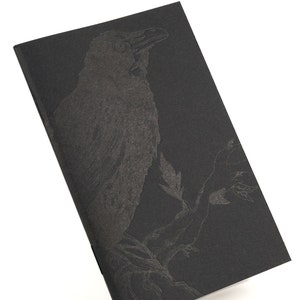 May include: A black notebook with a silver embossed image of a crow perched on a branch.