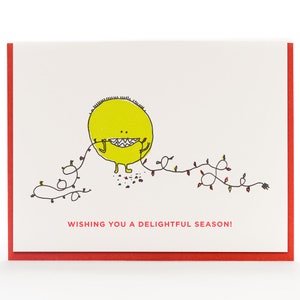 May include: A yellow monster with a toothy grin is tangled in a string of Christmas lights. The text "Wishing you a delightful season!" is below the monster.
