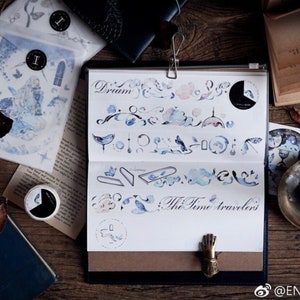 May include: A set of watercolor-style washi tape featuring a blue and white color scheme. The tape includes designs of clouds, birds, and other whimsical elements. The text "The Time Travelers" is written on the tape.