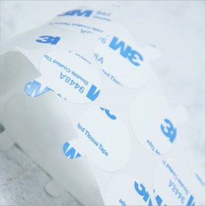 May include: A roll of white, round, adhesive stickers with blue text that reads "3M 9448A Double Coated Tissue Tape".