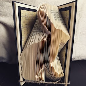 May include: A book art sculpture of a dog made from the pages of a book. The sculpture is made by folding the pages of the book into a three-dimensional shape.