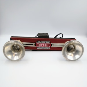 Könnte beinhalten: Vintage-Blitzgerät in Rot und Schwarz mit zwei silbernen Reflektoren. Das Gerät trägt den Text "with exclusive exposure spindal mov-e-lite home-lite manufacturing co. chicago".