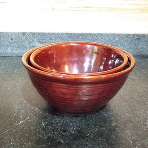 May include: A set of two brown ceramic mixing bowls. The larger bowl is nested inside the smaller bowl.