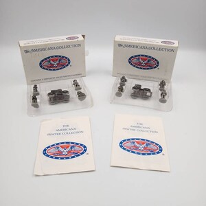 May include: Two unopened boxes of The Americana Collection pewter figurines. Each box contains five different solid pewter figurines. The boxes are white with blue and red accents. The boxes are on a white surface.